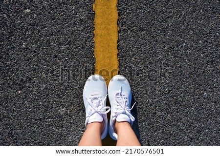 Feet and legs standing in the middle of the yellow road line visible from above, great selfie for any use.