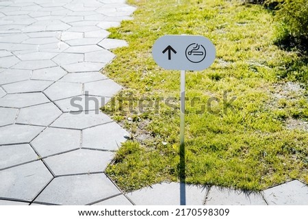 Arrow pointer on the banner smoking area, cigarette painted on a white sign, pedestrian zone, information stand on the lawn. High quality photo