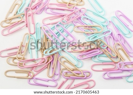 Multicolored paper clips scattered as textured background in full screen. Stationery concept.