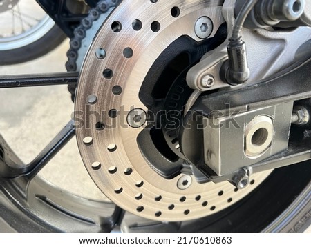 Close-up of motorcycle disc metal, metal surface with small round vents, black aluminum wheels as background.