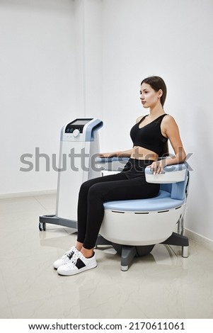 Young woman sitting on electromagnetic chair for stimulation of deep pelvic floor muscles and restoring neuromuscular control at the clinic Royalty-Free Stock Photo #2170611061