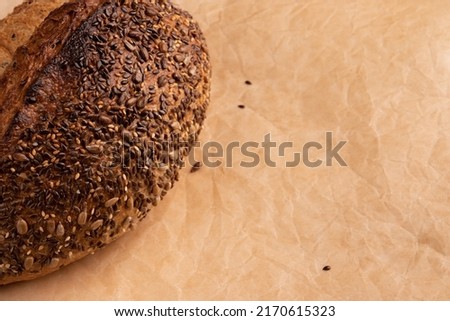 top view of fresh homemade bread with golden crispy crust on parchment for baking, organic loaf with sunflower and linen seeds close-up and space for text