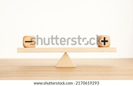 Plus and minus balance concept. Positive and negative symbols on wooden blocks are in balance on a wooden seesaw. Copy space