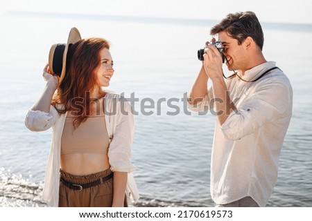 Side view beautiful young couple two family man woman in white clothes boyfriend take photo on camera of girlfriend rest date at sunrise over sea sand beach ocean outdoor seaside in summer day sunset