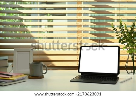 Digital tablet with wireless keyboard, coffee cup, books and picture frame on white table