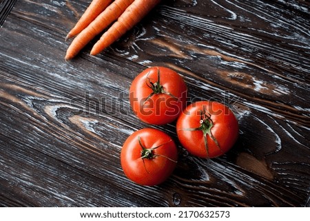 Appetizing composition of fresh vegetables, carrots and tomatoes on a wooden dark textured table.