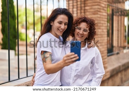 Two women mother and daughter hugging each other using smartphone at street