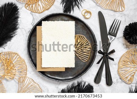 Black and golden wedding table setting with a place card and rings top view, mockup. Elegant flat lay with handmade paper card, wedding or holiday stationery template