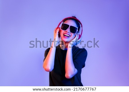 Young asian girl in black t-shirt wearing sunglasses and red headphones listen to music and dancing on purple background.