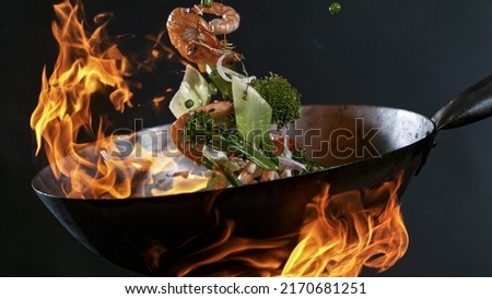 Freeze Motion of Wok Pan with Flying Ingredients in the Air and Fire Flames. Royalty-Free Stock Photo #2170681251