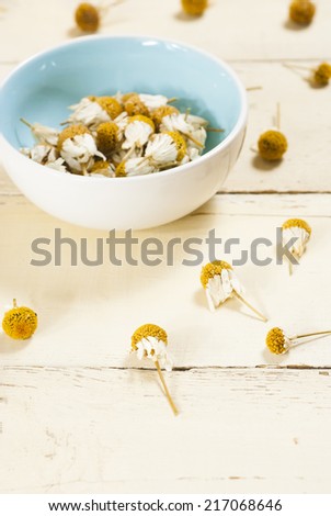 dried chamomile flowers in a blue china bowl, rusty white wood table background