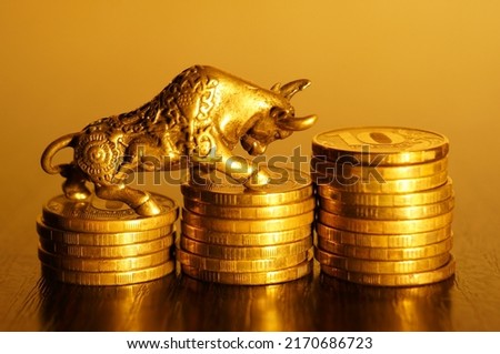 Metal bull with coins on a gold background. A symbol of financial success and independence.