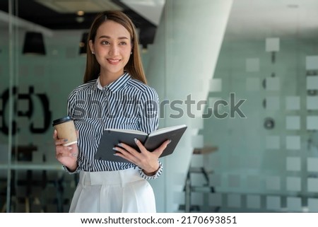 business woman standing with a notebook in the office and drinking coffee