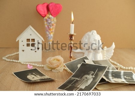 stack of vintage photos on table, romantic still life in love style, in glass vase red hearts on sticks, model house, candles burning, concept of family tree, genealogy, childhood memories