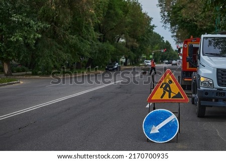 Repair of the city road. Detour obstacles. Repair machines. A man with a wheelbarrow is walking along the highway.