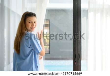 Asian nurse open the curtains in the living room to allow light to reach the room before bringing the patient to sit in this living room.