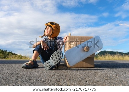 Cute dreamer little girl playing with cardboard planes on a lake road on a sunny day. Happy kid playing with cardboard plane against blue summer sky background. Childhood dream imagination concept. Royalty-Free Stock Photo #2170717775
