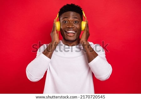Photo of astonished cheerful person hands touch headphones isolated on red color background
