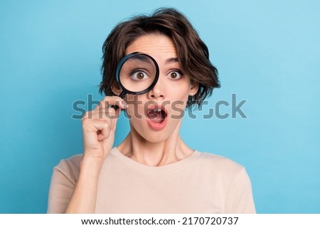 Photo of young impressed young lady using magnifying glass play detective catch spy isolated on blue color background