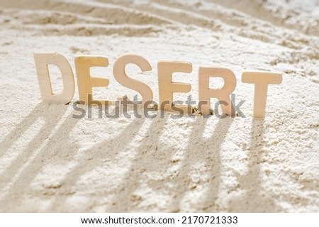 wooden letters make up the word desert inserted in the sand. shadows on the sand