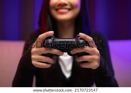 Close up hands Playing video game. Young pretty woman sitting on sofa holding joystick in living room. Female Professional Streamer  wearing hoodie playing game online in dark room neon light.