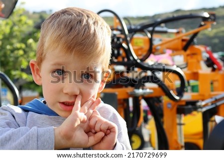 The blond boy holds his hands near his face and looks attentively into the distance. Thoughtful five-year-old boy.