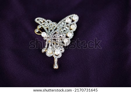 Pearl and diamond brooch in the shape of a butterfly isolated on a dark purple silk background Royalty-Free Stock Photo #2170731645