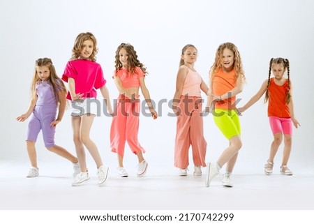Contemporary dances. Happy, sportive little girls, kids in bright colorful clothes dancing modern dance isolated on white studio background. Concept of music, fashion, art, childhood, hobby.
