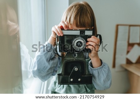 Unrecognizable little girl taking photo by vintage film camera indoor
