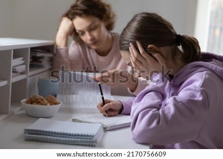 Upset mother and teenage daughter studying at home, sad unhappy teen girl doing school assignments, difficult task, routine boring homework, strict mother controlling lazy schoolgirl Royalty-Free Stock Photo #2170756609