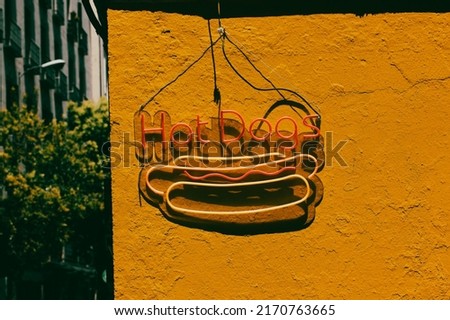 Hot dogs LED sign against yellow wall on street. Fast food bistro, cafe stylish exterior. Hot dog modern trendy neon label, icon. Design element, light banner, announcement. USA, American food snacks