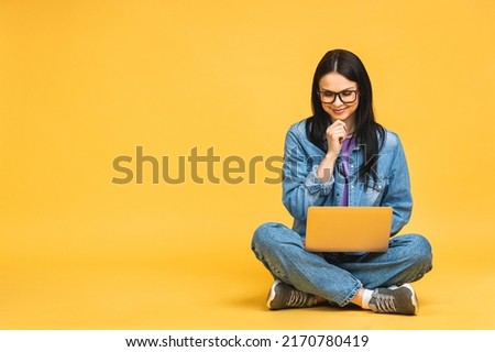 Business concept. Portrait of happy young woman in casual sitting on floor in lotus pose and holding laptop isolated over yellow background. Royalty-Free Stock Photo #2170780419