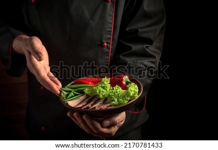 The chef brings a plate of chopped baked meat and vegetables. The concept of cooking on a dark background