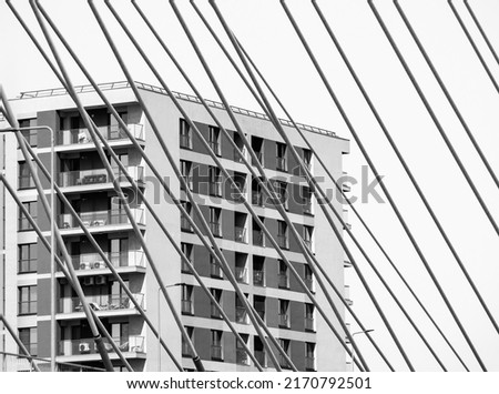 Black and white minimalist abstract picture with an apartment building in the background and  the metal bars or wires of a suspended bridge