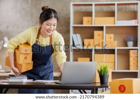 Startup SME small business entrepreneur of freelance Asian woman wearing apron using laptop and box to receive and review orders online to prepare to pack sell to customers, online sme business ideas. Royalty-Free Stock Photo #2170794389