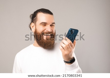 Close up photo of young bearded man talking on smarphthone via speacker.