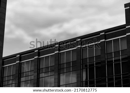 A low angle greyscale of a modern skyscraper under the cloudy sky