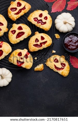 Mini halloween pumpkin hand pies with  strawberry jam. Jack-O-lantern cookies or pies on a black background. Halloween dessert. Top view. Copy space