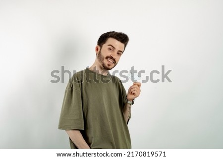 Happy casual man wearing t-shirt posing isolated over white background holding credit card and smiling with a confident smile showing teeth.