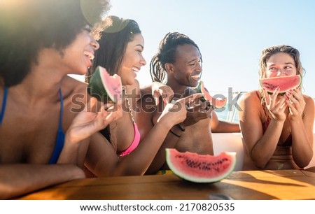 Group of multicultural young  having a tour on boat and eating fresh watermelon while the girl with blonde hair joking with slices of fruit- focus on the head of blonde girl