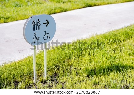 Sign with an arrow towards the toilet, a public restroom for the disabled, a mother-and-child room, a lawn banner, a city toilet, a road in the park. High quality photo
