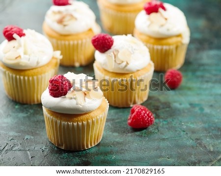 Many muffins with cream, raspberries and almonds on a dark green background. Holiday, banquet, picnic. Holiday invitation, advertisement, banner. There are no people in the photo.