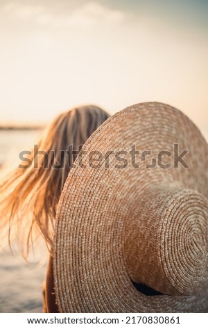 Young beautiful woman in a black swimsuit and hat with glasses walks along the beach in Turkey at sunset. The concept of sea recreation. Selective focus
