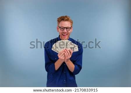 Funny rich man with a fan of dollars, sniffing money isolated on a blue background