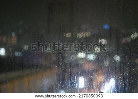 Rain drops on the window. Rain drops on the glass on a background of a night blurred city. Rainy weather. Outside the window is a blurred city. Bokeh night city. unfocus