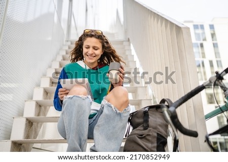 One woman female student sitting on the stairs by the university building holding digital tablet and cup of coffee happy smile in day copy space