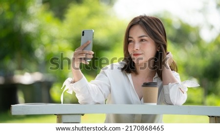 Thoughtful smile woman in park using smart phone for selfie photo , Portrait of a young charming business woman checking online Business work on her smart phone outdoors in the park on soft green 