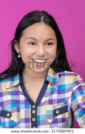 face of young latin girl with asian features with long black hair and a plaid shirt, model beauty smiling in studio with colorful background