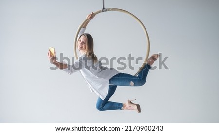 Caucasian woman gymnast on an aerial hoop takes a selfie on a smartphone. 