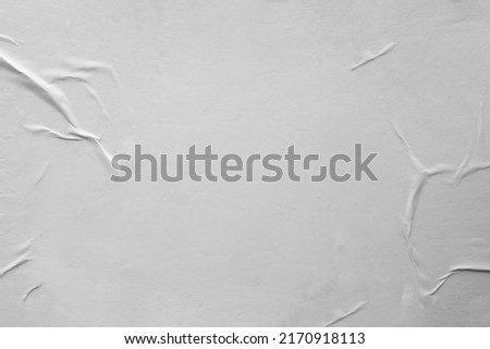 Blank white crumpled and creased paper. White sheet of crumpled paper glued to the wall. Beautiful abstract artistic white empty street poster paper texture pattern